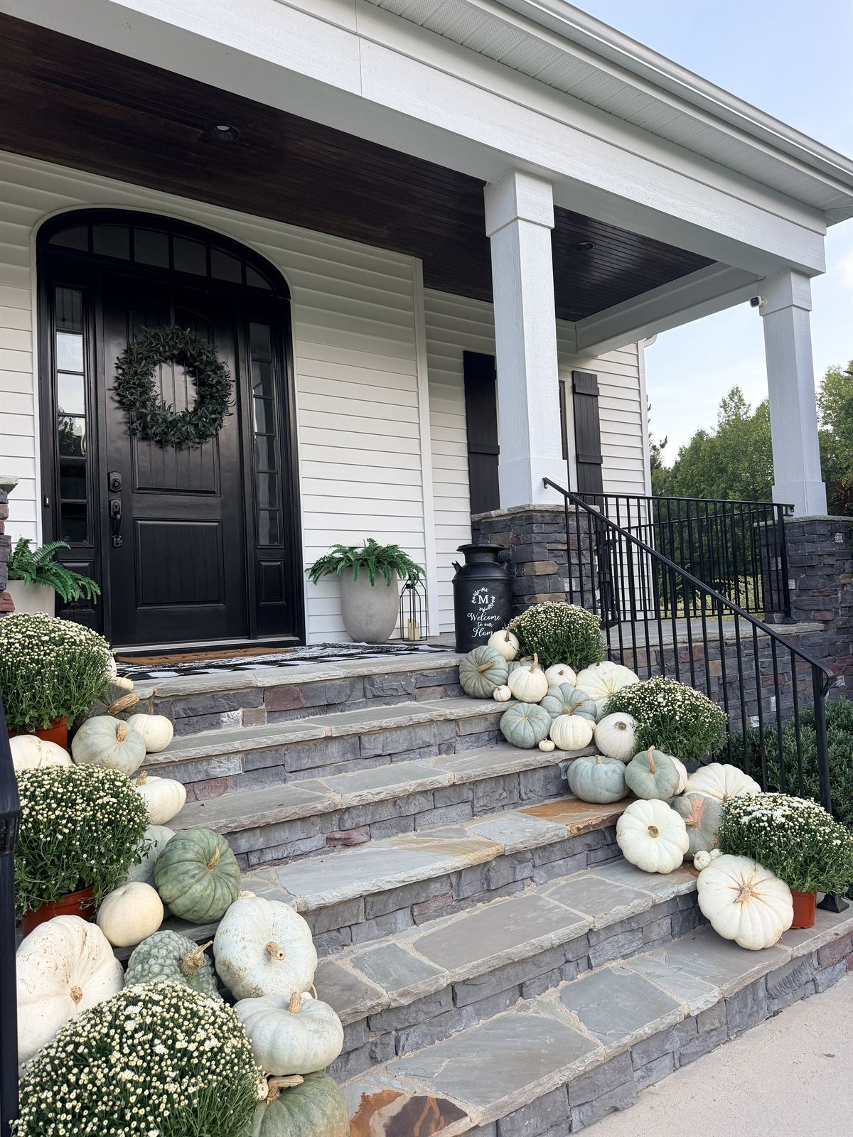 White farmhouse porch with a black arched door and stone steps lined with white mums and white and sage heirloom pumpkins, Triangle NC