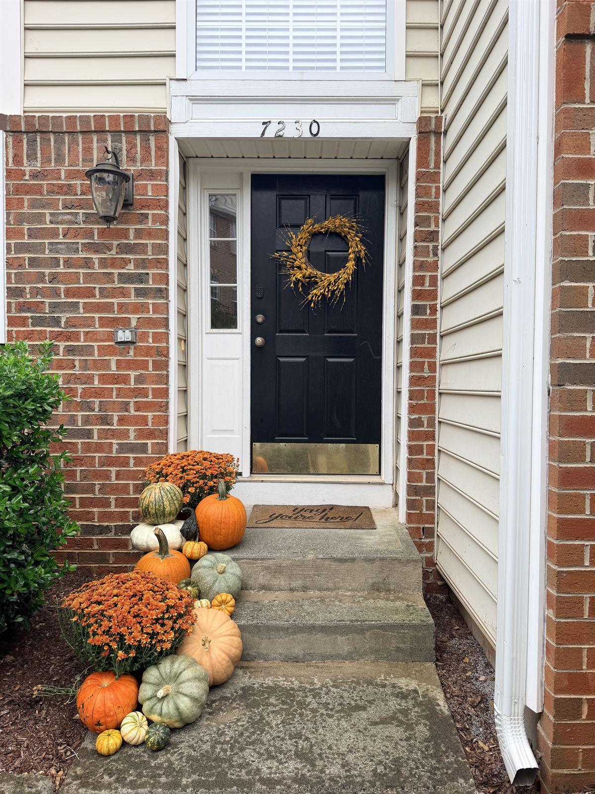 Brick townhouse entry with a black door and fall wreath, orange mums and orange, white and sage pumpkins on the steps, Cary NC area